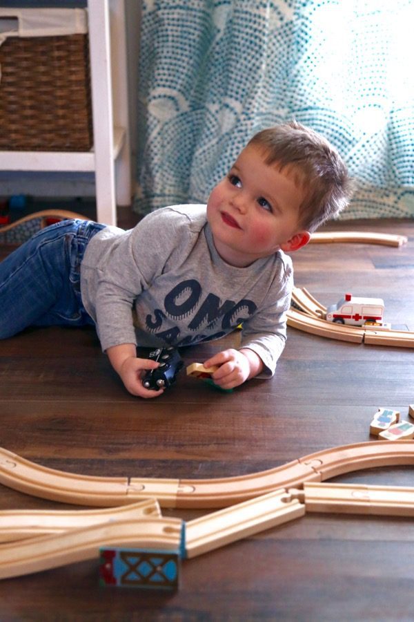 A small boy laying on the floor playing with trains 