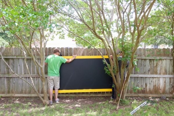 man hanging outdoor chalkboard on a fence