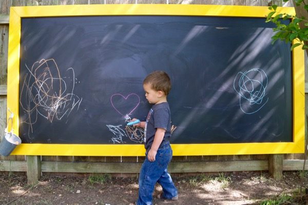 toddler coloring on an outdoor chalkboard