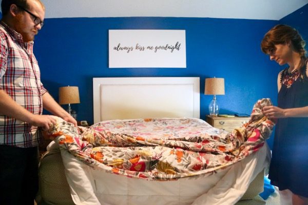 A man and woman putting a duvet cover back on a bed