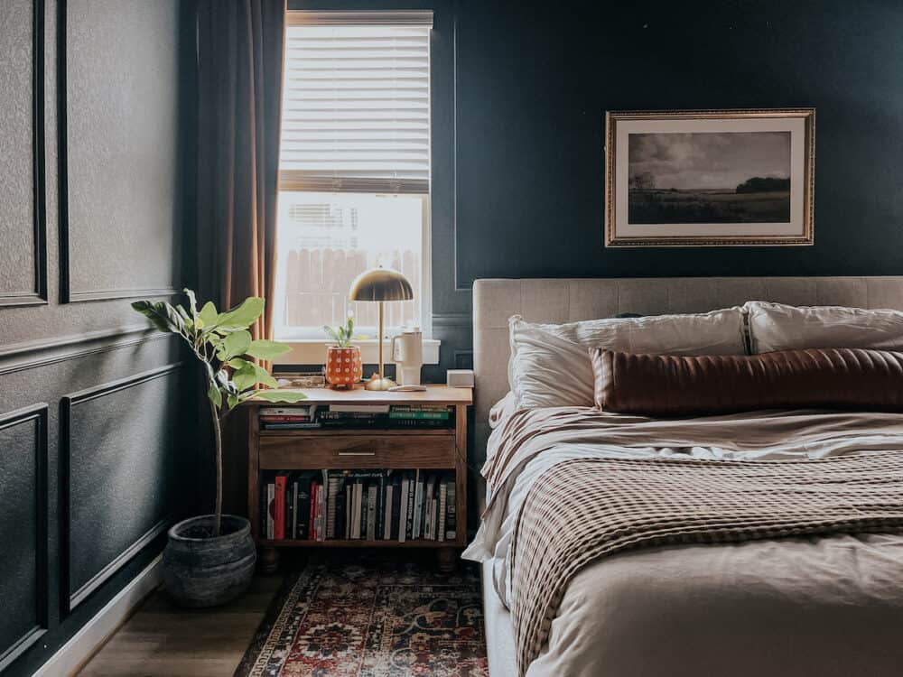 a cozy bedroom with dark walls and an art print hanging above the bed 