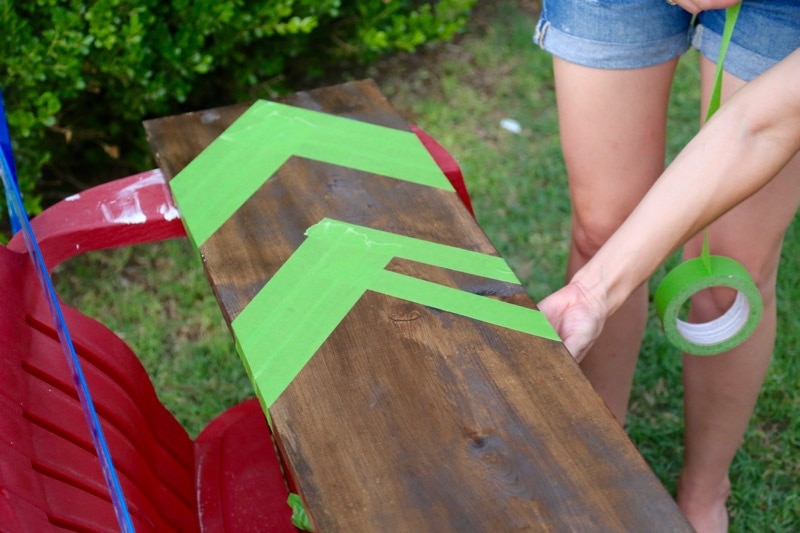Woman taping chevron-shaped stripes on a piece of wood