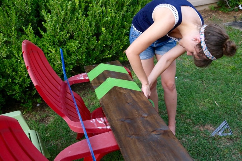 woman taping off chevron stripes on a piece of wood to create a growth chart ruler