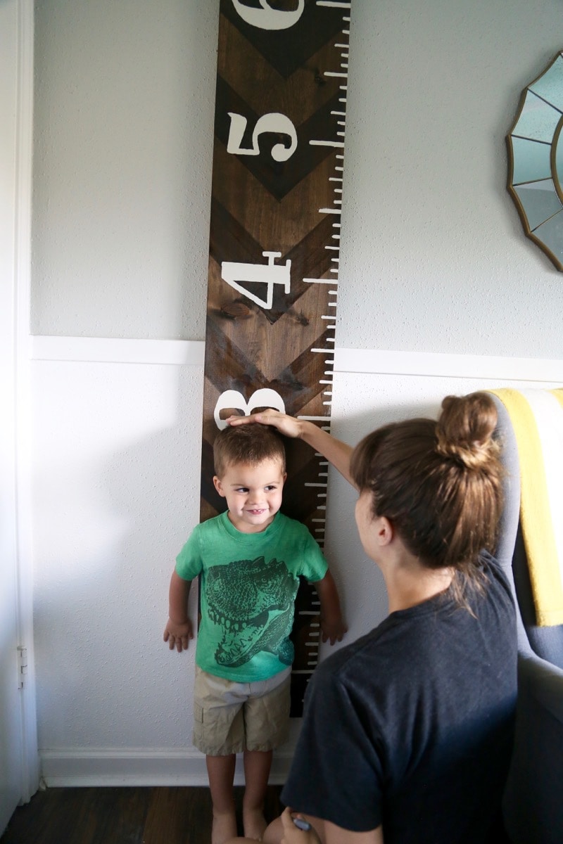 A toddler being measured on a wooden growth chart