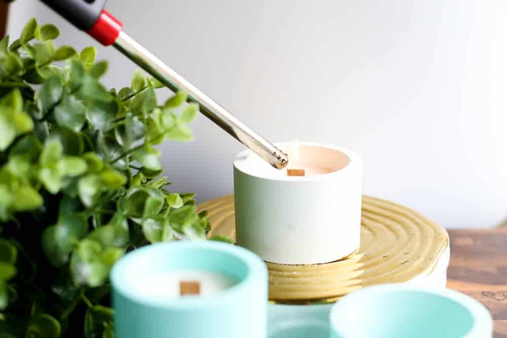 Three homemade candles and DIY concrete candle holders on a table, with one candle being lit