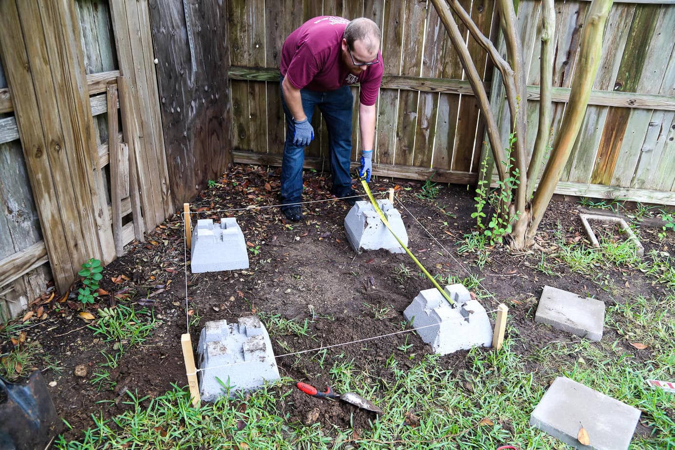 man planning and measuring for concrete footings for DIY outdoor playhouse