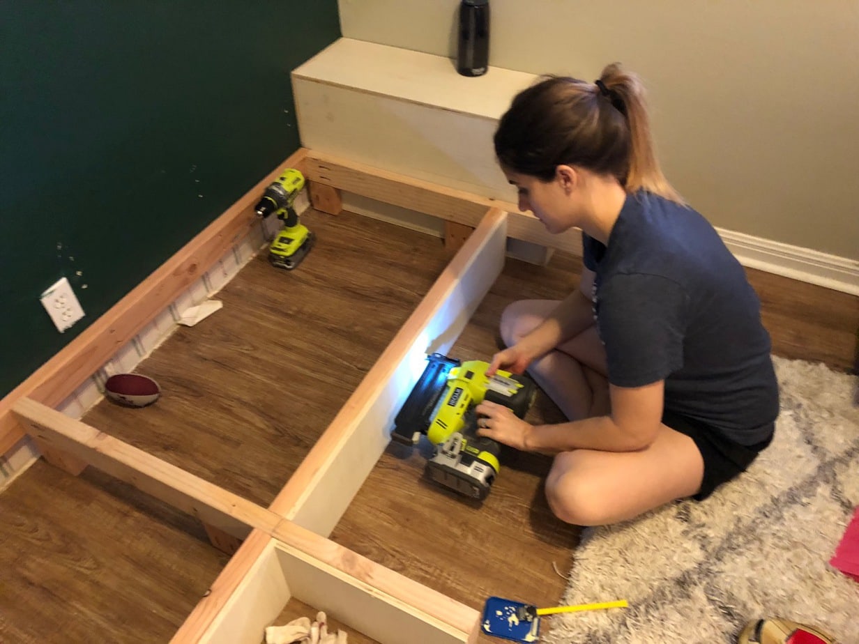 Woman nailing plywood to framing for DIY built in shelves