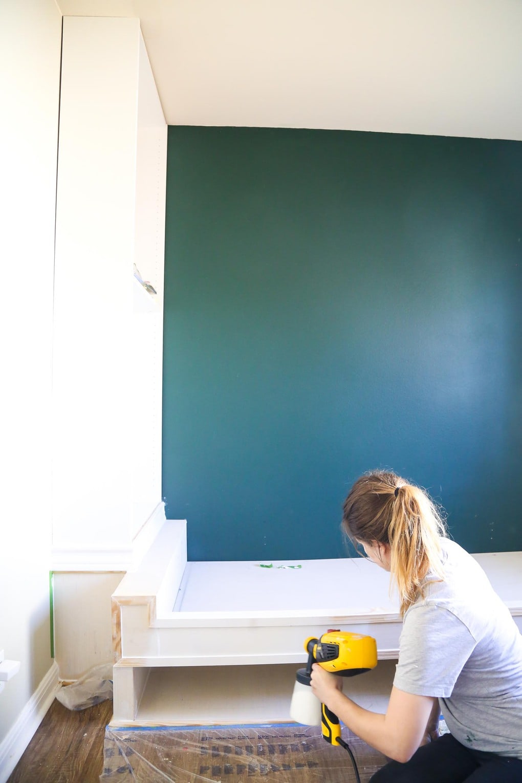 Woman using paint sprayer to paint DIY build in shelves