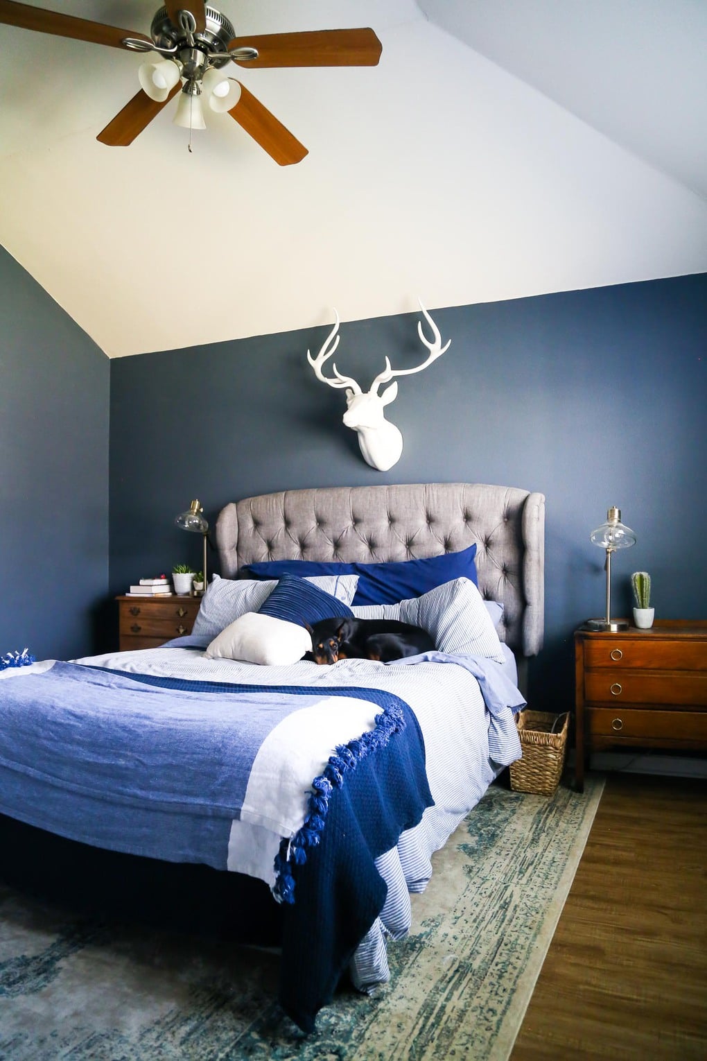 A master bedroom with dark blue walls, blue bedding, and Mohawk vinyl plank flooring