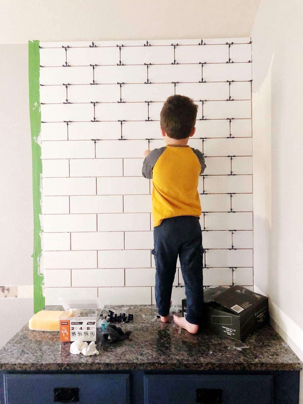 young boy removing spacers from a tile backsplash