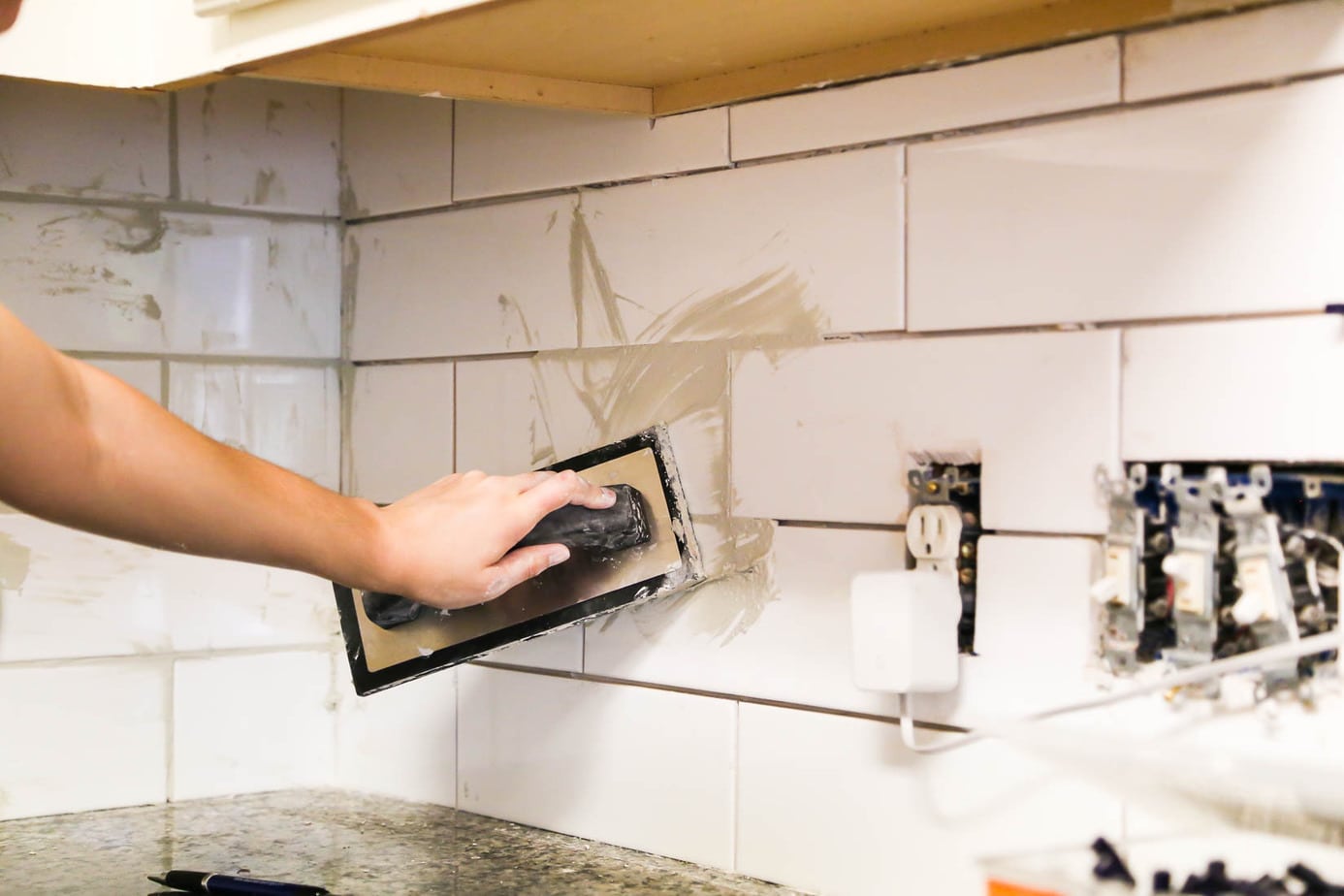 hand applying grout to a backsplash