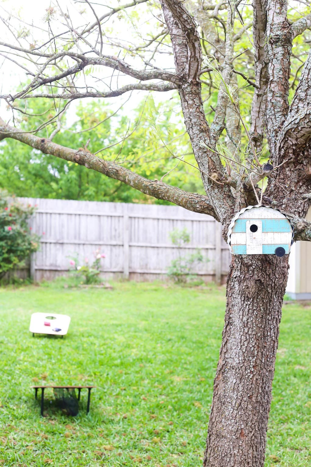 Tree with camper-shaped bird house and backyard games in the background