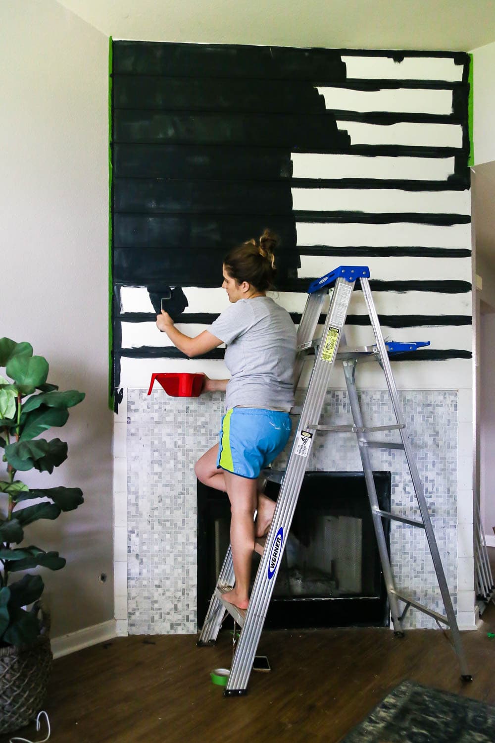 woman using a paintbrush to paint a shiplap fireplace wall black