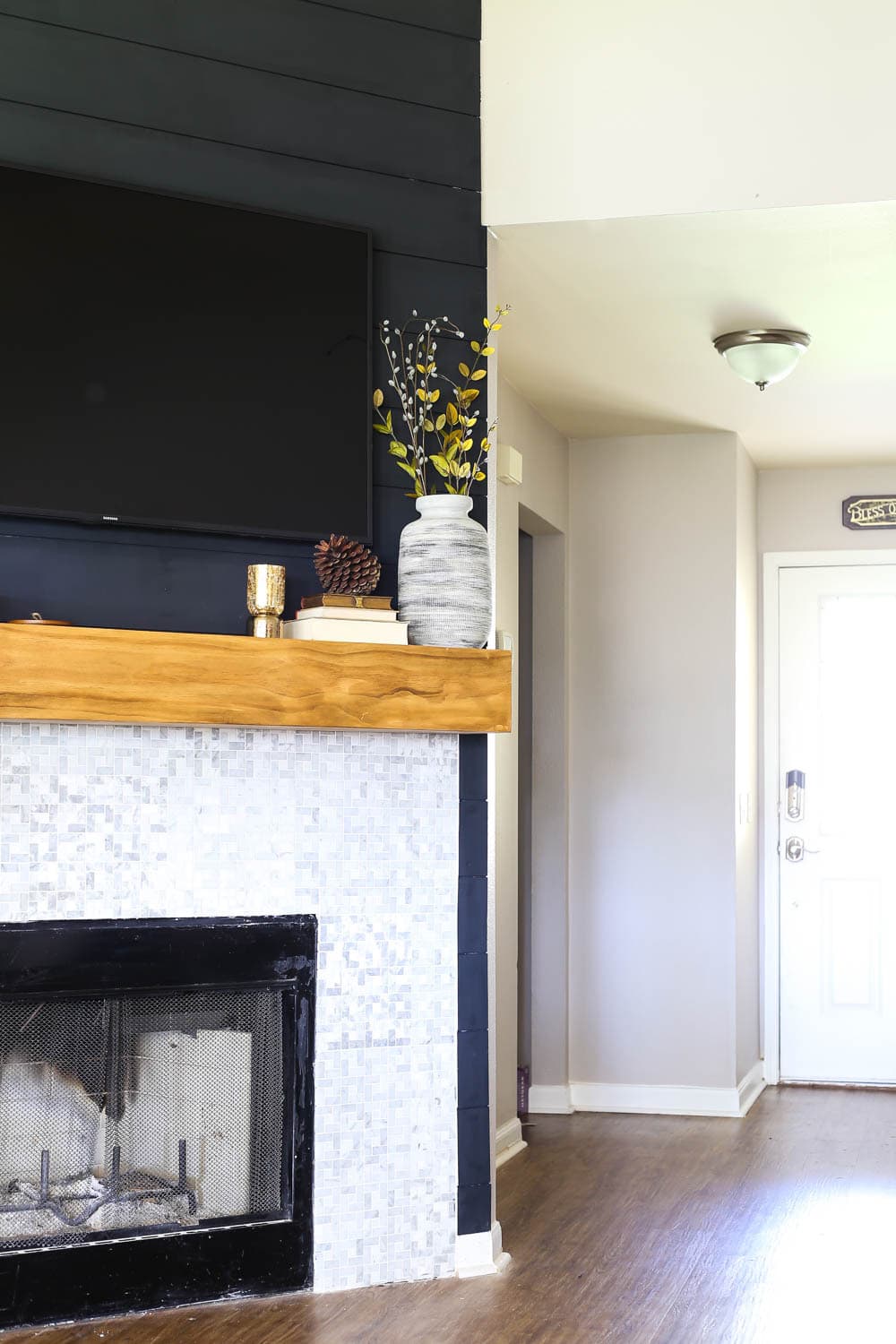 a living room fireplace with black shiplap, a wood mantel, and marble tile