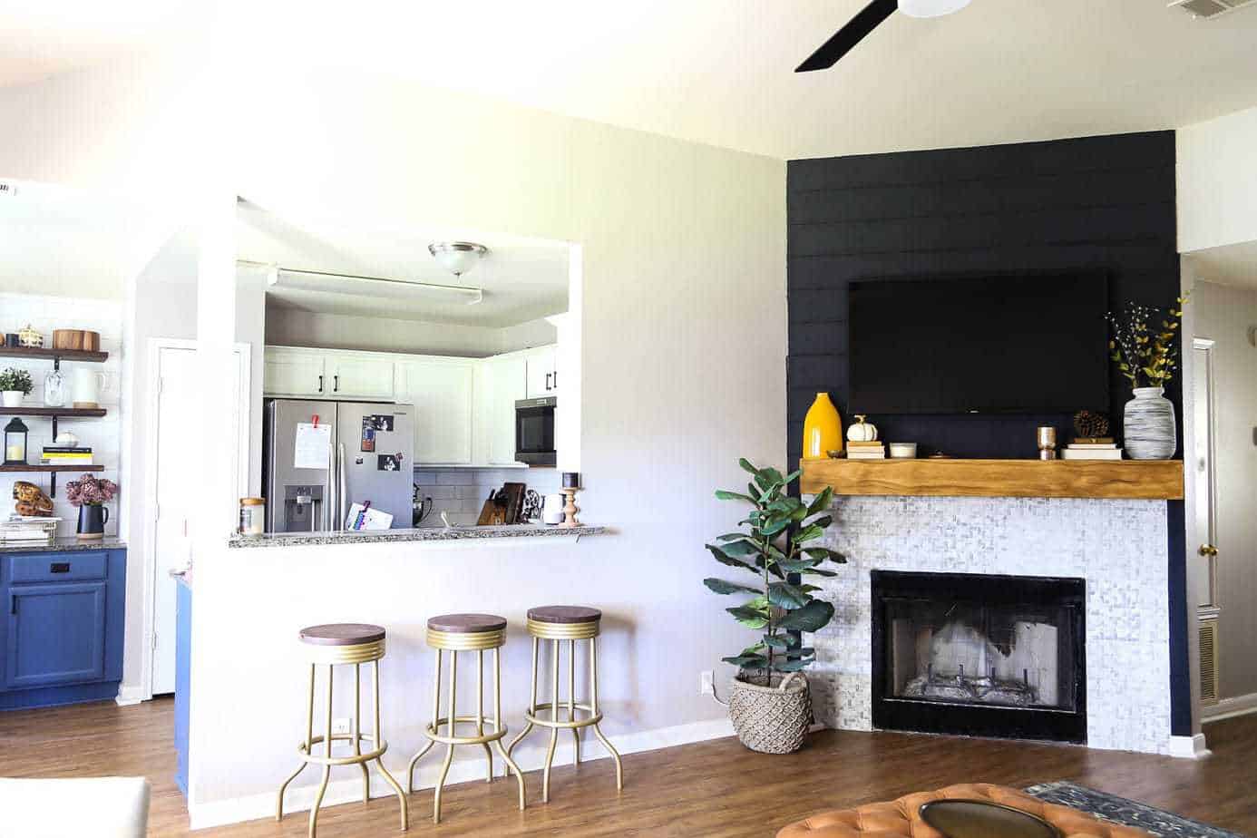 living room with a black shiplap fireplace in the corner and gold barstools near the kitchen