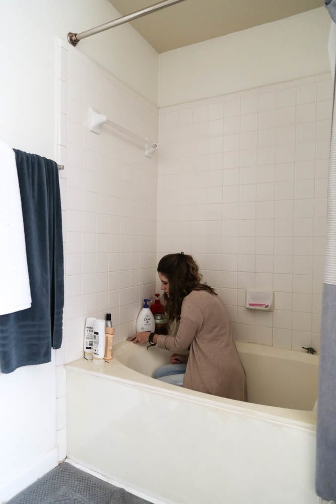 woman removing caulk on a bathtub and shower surround