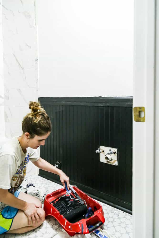 woman painting beadboard paneling in bathroom white