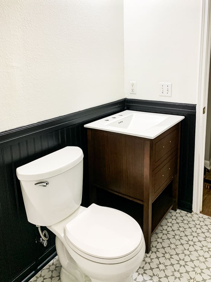 bathroom with vanity and toilet installed and black and white walls with gray patterned tile.