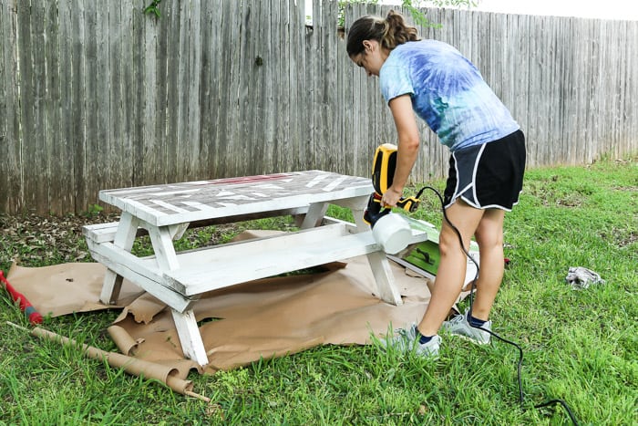 woman using paint sprayer to paint a picnic table