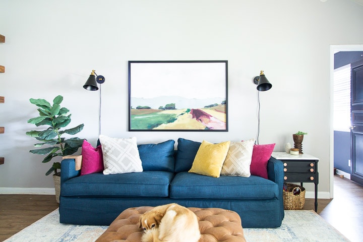 living room with a blue sofa, landscape art, and black sconces