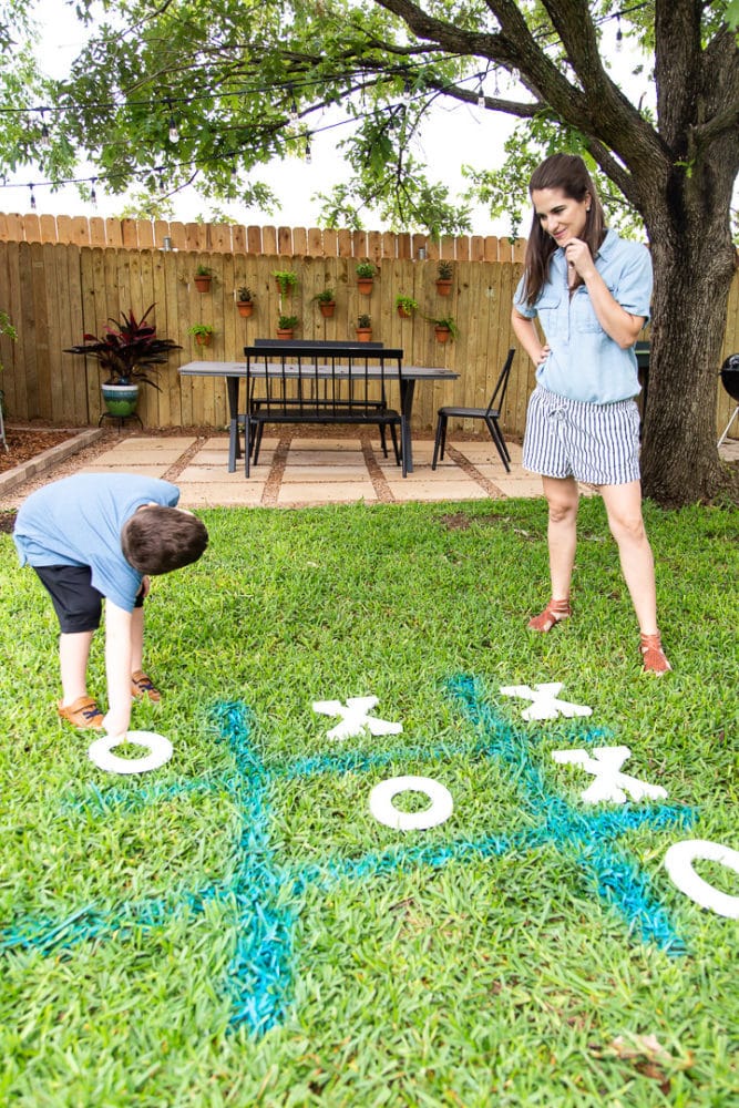 a mom and her young son playing tic tac toe in the grass using spray chalk