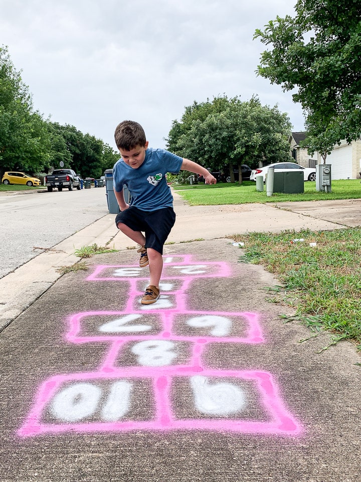 young boy playing hopscotch on the sidewalk