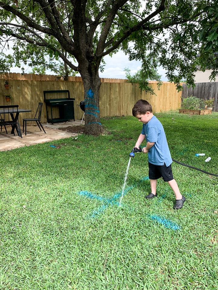 a young boy cleaning up spray chalk using a water hose