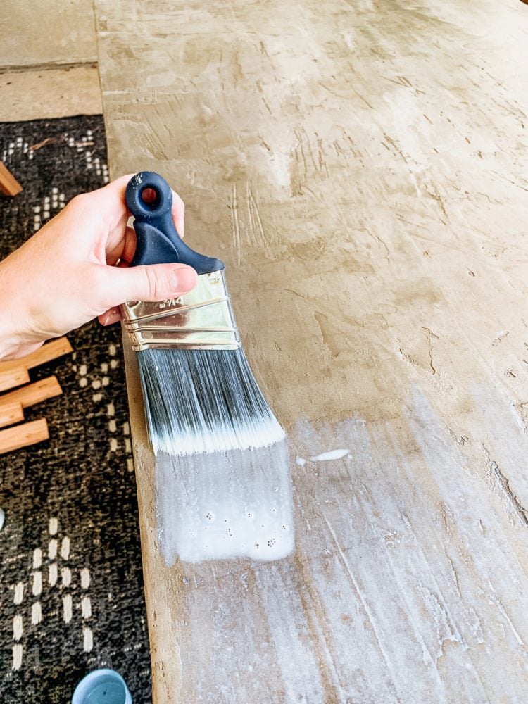 hand with a paintbrush applying concrete sealer