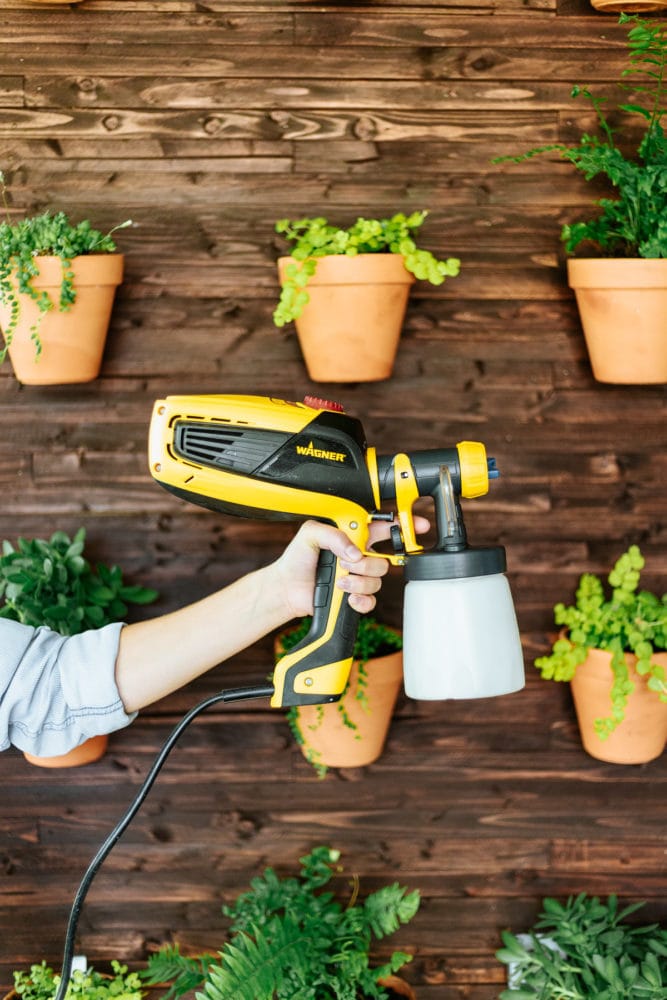 woman's hand holding a paint sprayer in front of a DIY plant wall