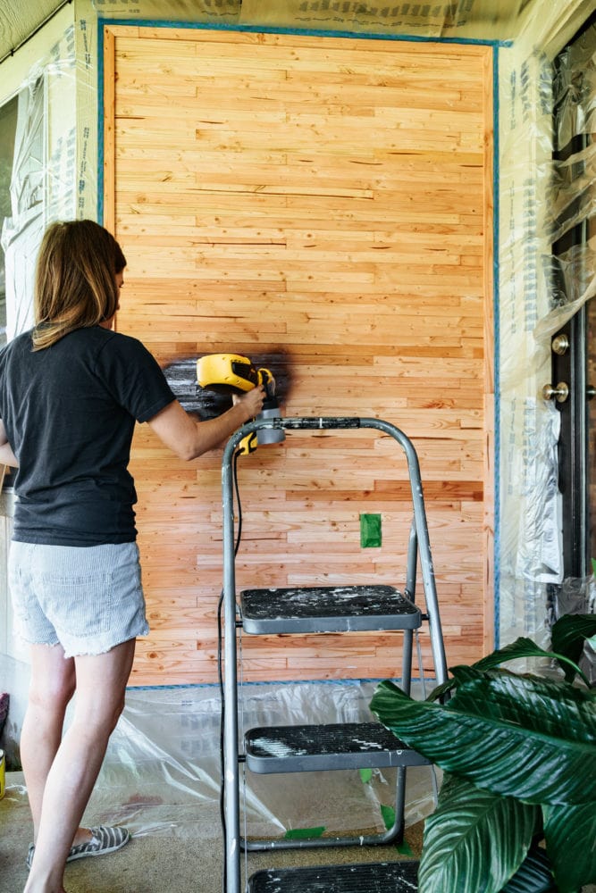 woman staining a wall with a paint sprayer