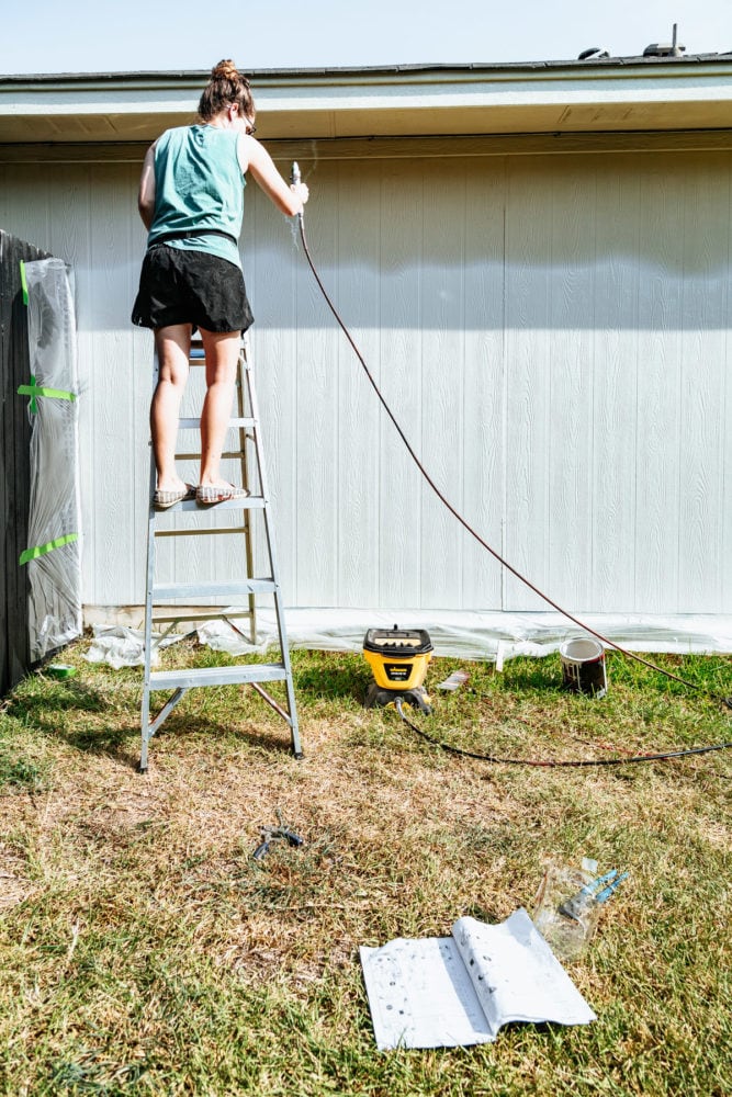 woman using a paint sprayer to paint the exterior of a house