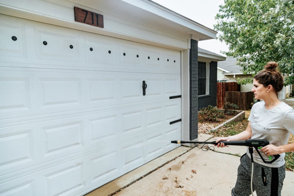 woman using a pressure washer to clean a garage door