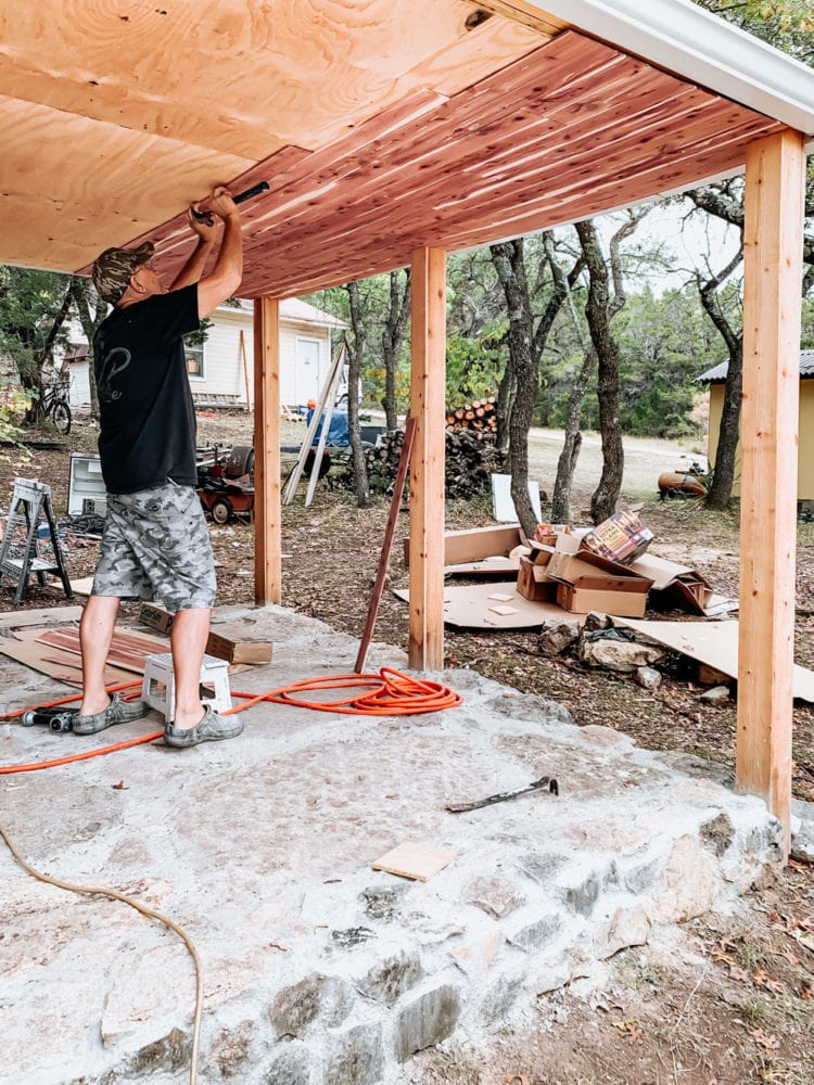 man nailing a cedar plank into the underside of an exterior pergola