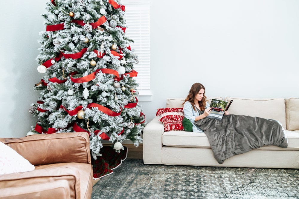 Woman on a couch next to a large Christmas tree 