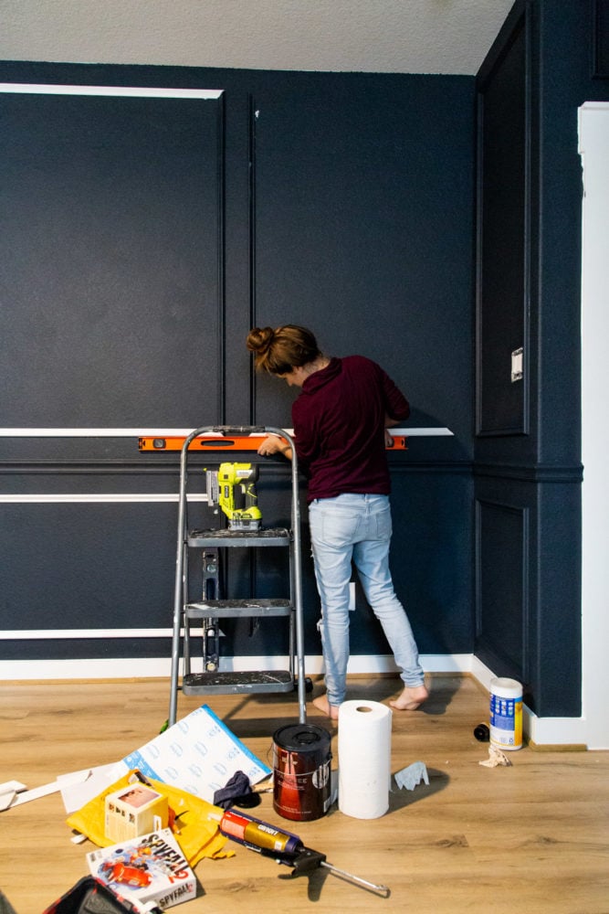 woman installing picture frame moulding in master bedroom