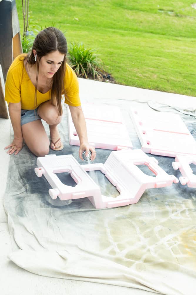 woman spray painting a plastic dollhouse