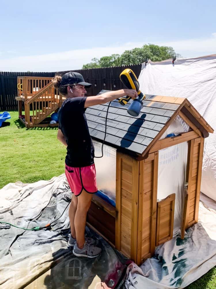woman painting a playhouse with a paint sprayer