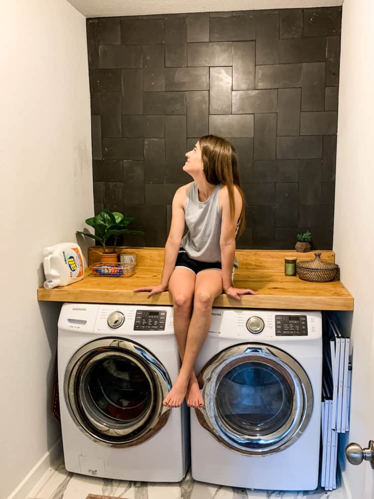 Woman sitting on a counter in a laundry room with a tiled basalt wall
