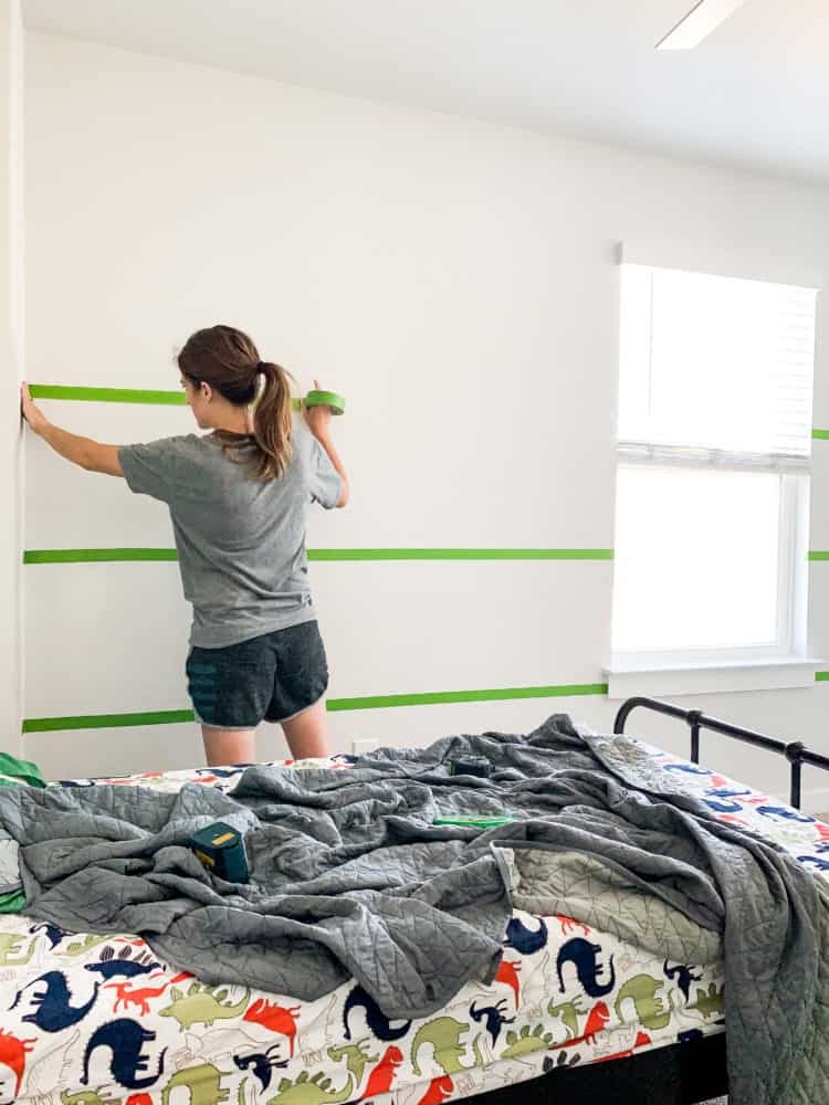 woman putting FrogTape on a wall to paint stripes