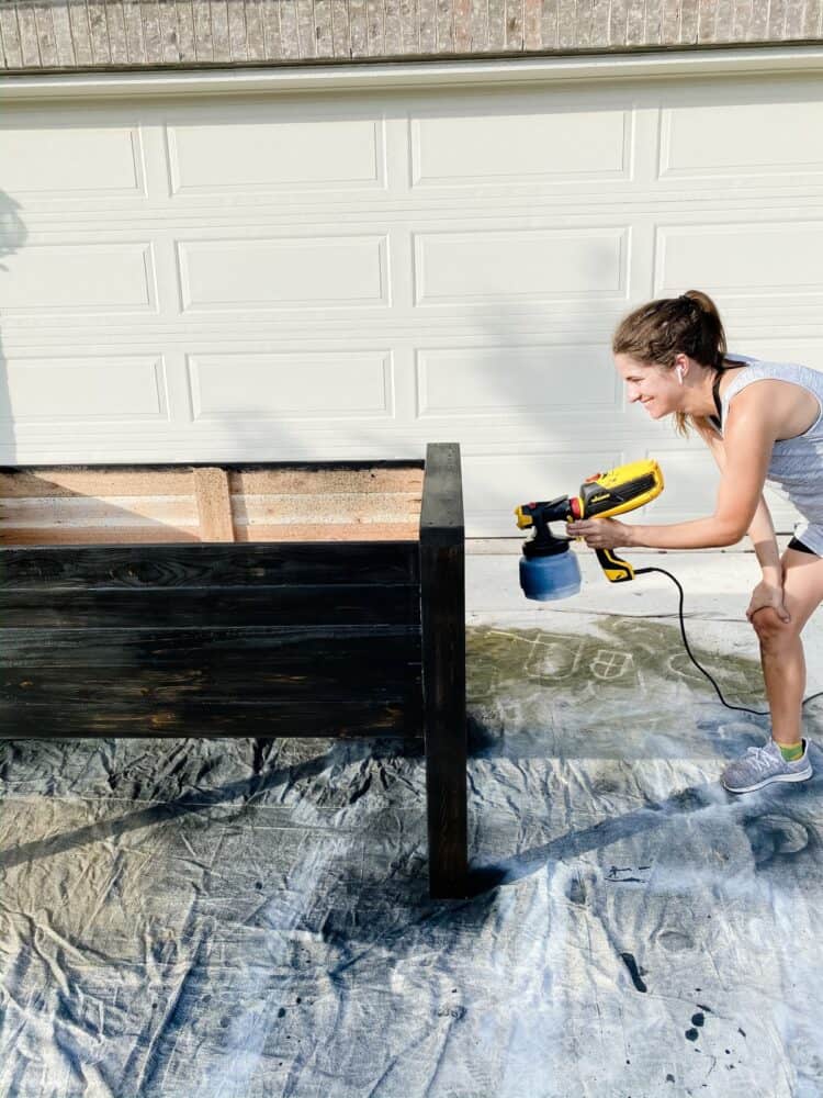 woman staining a garden bed with a paint sprayer
