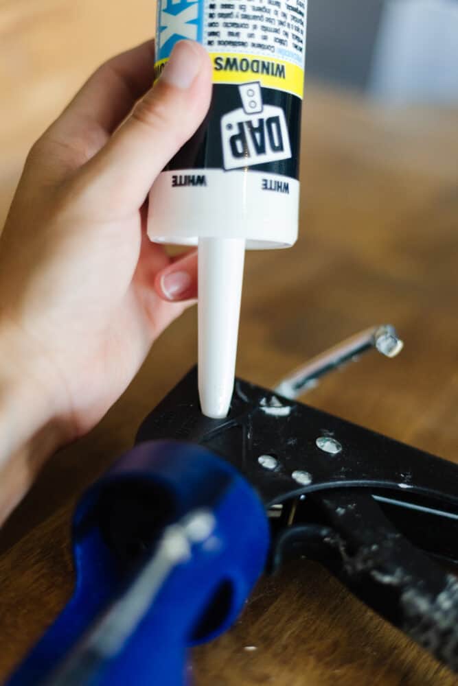 Hand holding the tip of a tube of caulk in the opening for the caulk gun