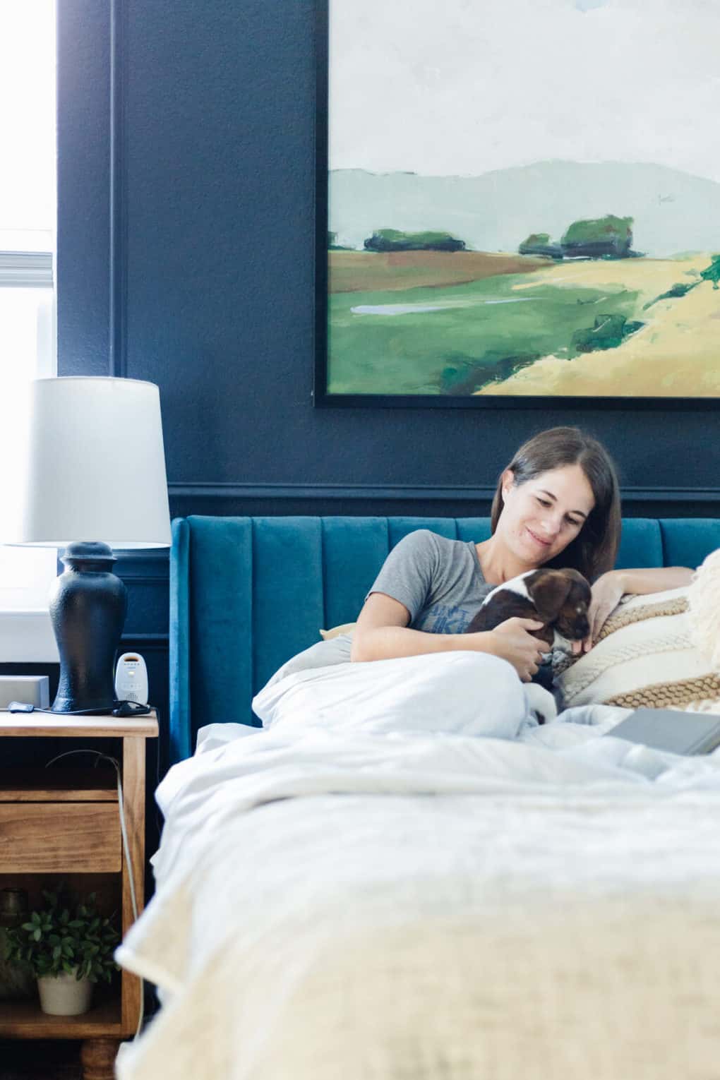 woman sitting on a bed using a weighted blanket and playing with a small puppy