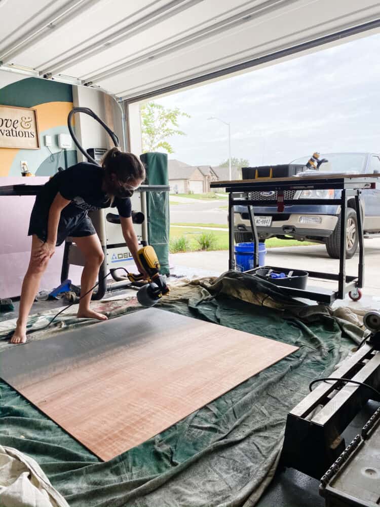 woman painting a large sheet of plywood using a paint sprayer