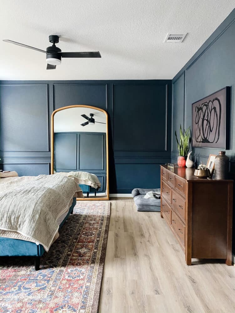 a dark blue bedroom with trim on the walls, a large mirror, and a wall-mounted television with hidden cords 