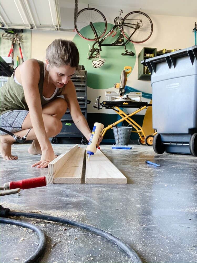 Woman adding wood glue to a board for the back of a DIY art ledge 