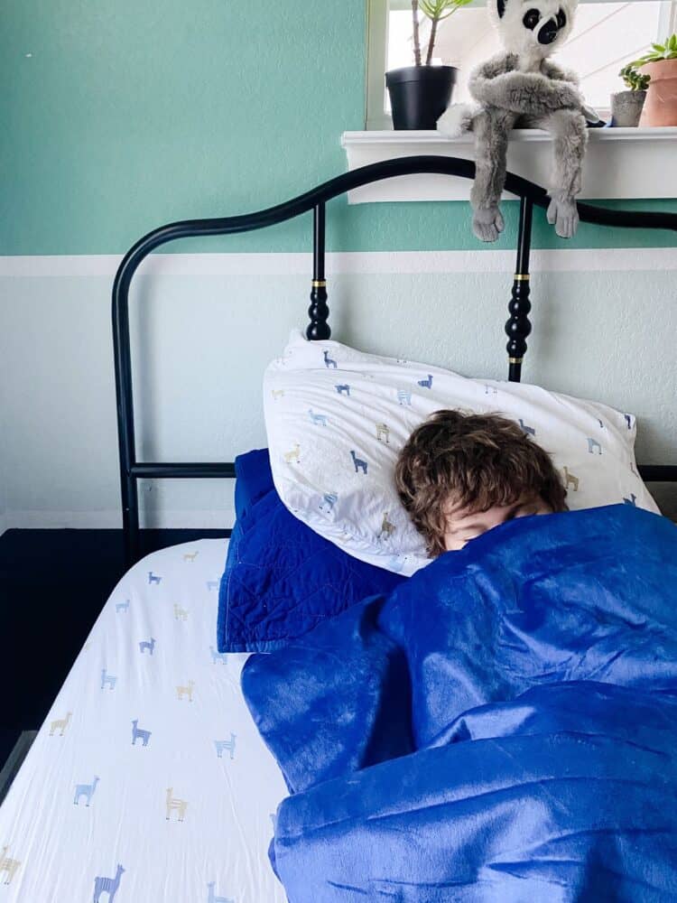 a young boy sleeping with a weighted blanket on top of him