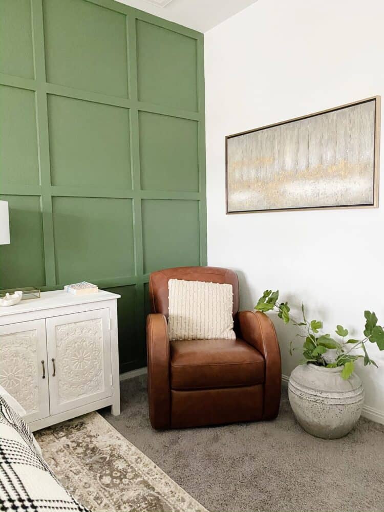 corner of a green and white bedroom with a leather chair, art, and a large vase 