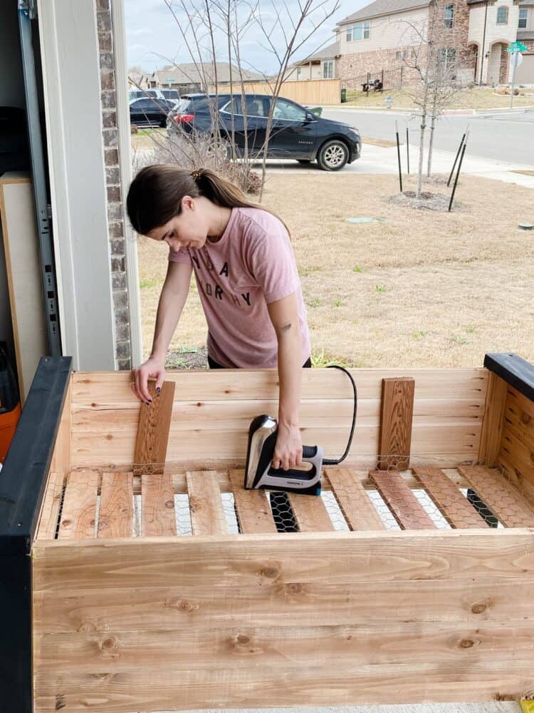 Woman using a staple gun to attach chicken wire to DIY garden bed 