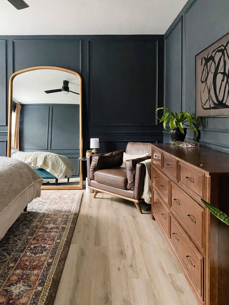 Master bedroom with dark walls and trim, a huge gold mirror, and a cozy leather chair 