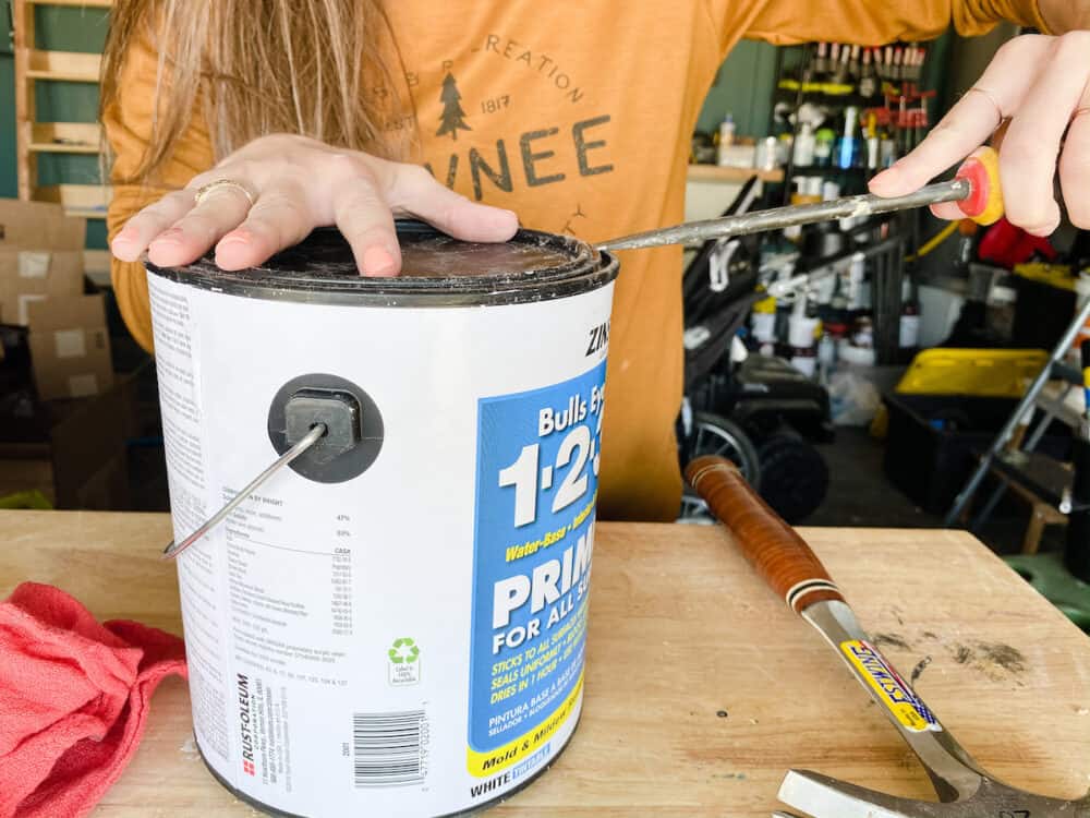 Close up of a paint can with a woman using a screwdriver to open it 